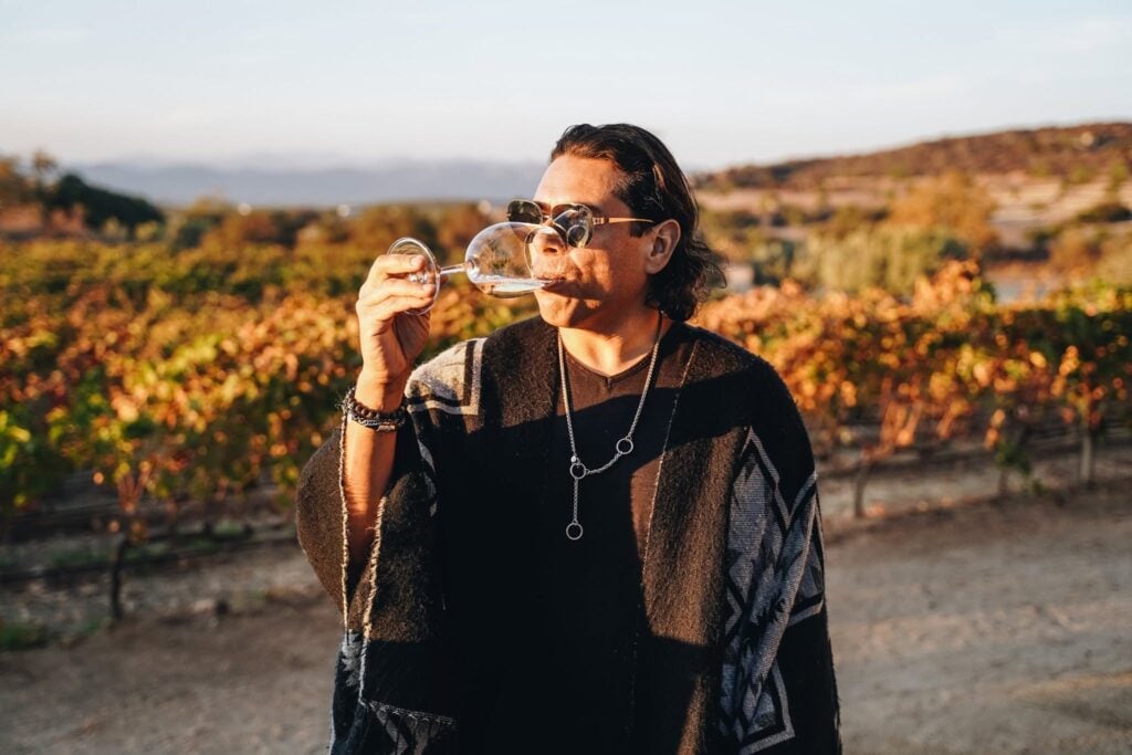 Fernando Gaxiola drinking wine, with a vineyard in the background