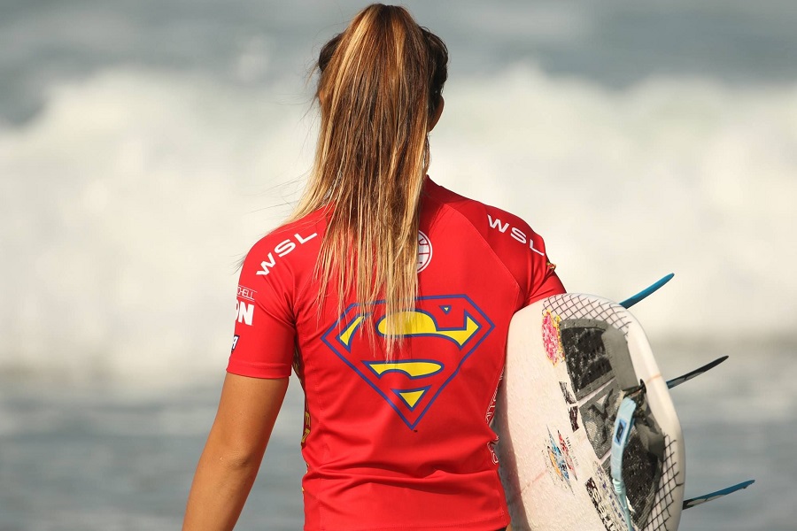 woman carrying a surfboard and wearing a superman shirt